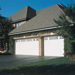 Two white garage doors on a house with a brick pattern.